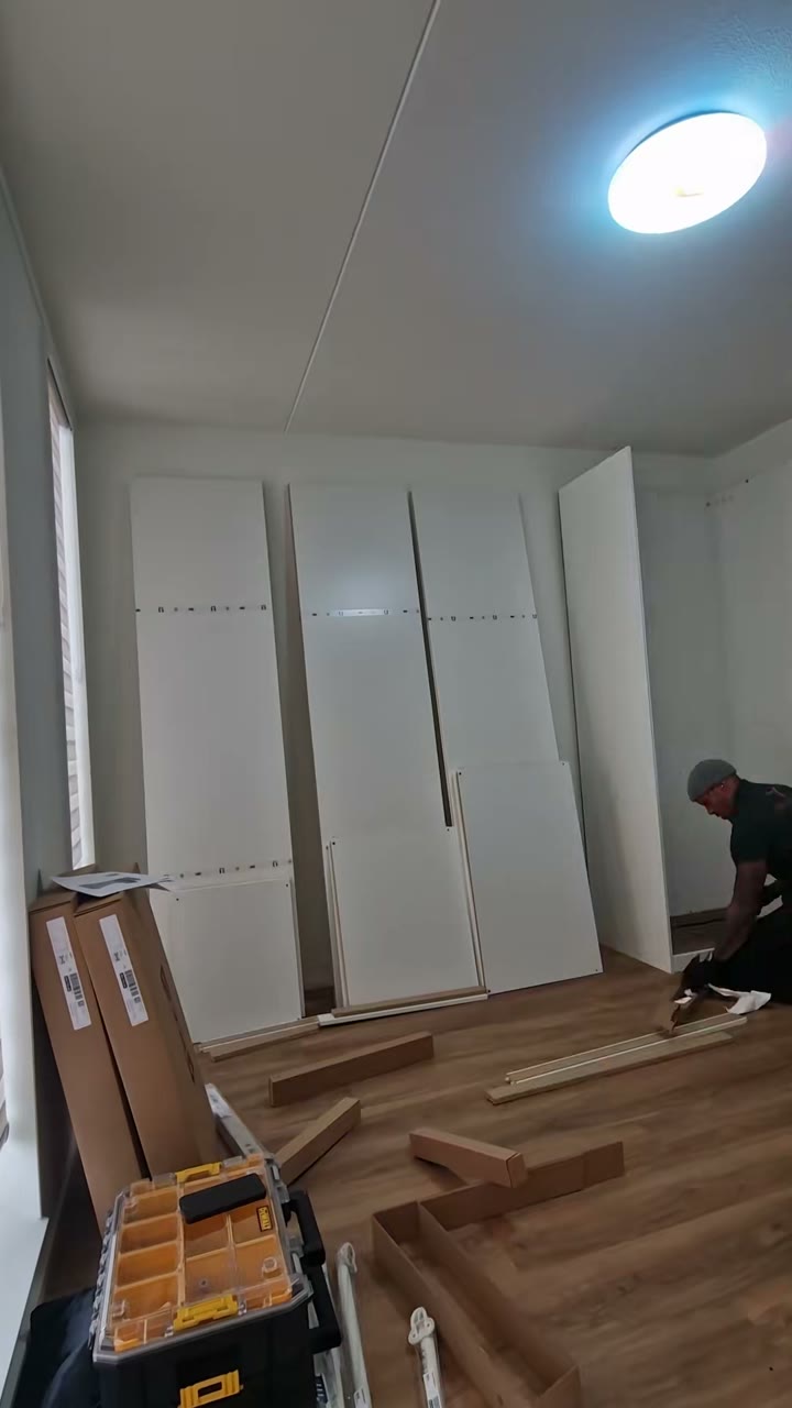 PAX-frames liggen en staan in een lege slaapkamer tijdens de montage, met gereedschap op de vloer