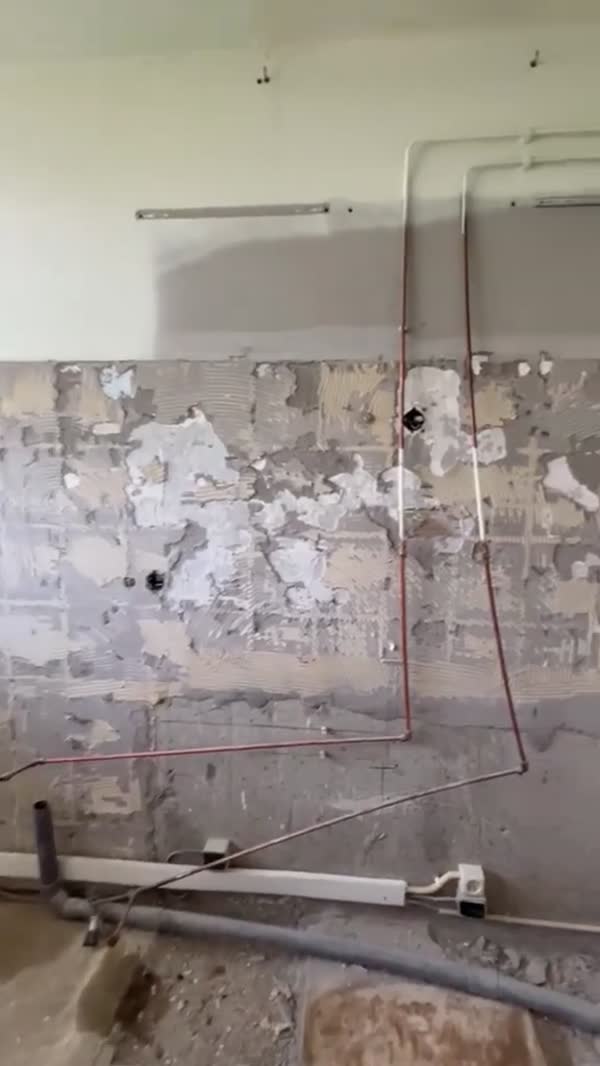 Gesloopte keukenwand met losse tegelresten en koperen leidingen